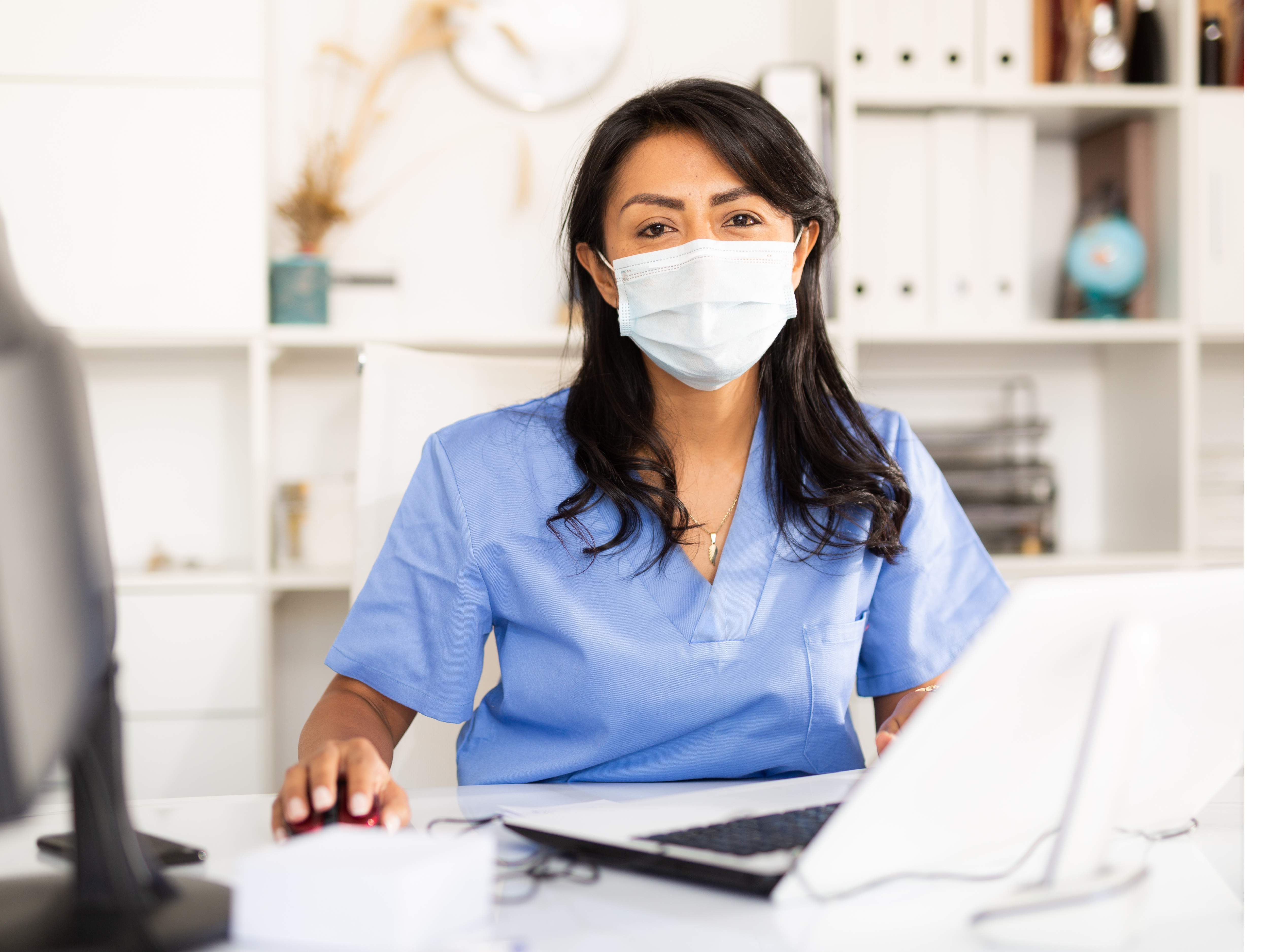 A female physician working on her laptop while wearing a mask.