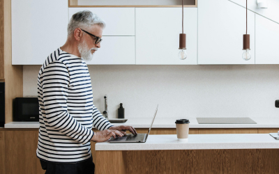 Man with glasses and a striped shirt working on a laptop in a modern kitchen setting, with a coffee cup placed nearby.