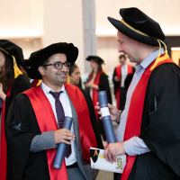 Two graduates talk to each other while carrying their diplomas during the Brisbane College Ceremony 2025.
