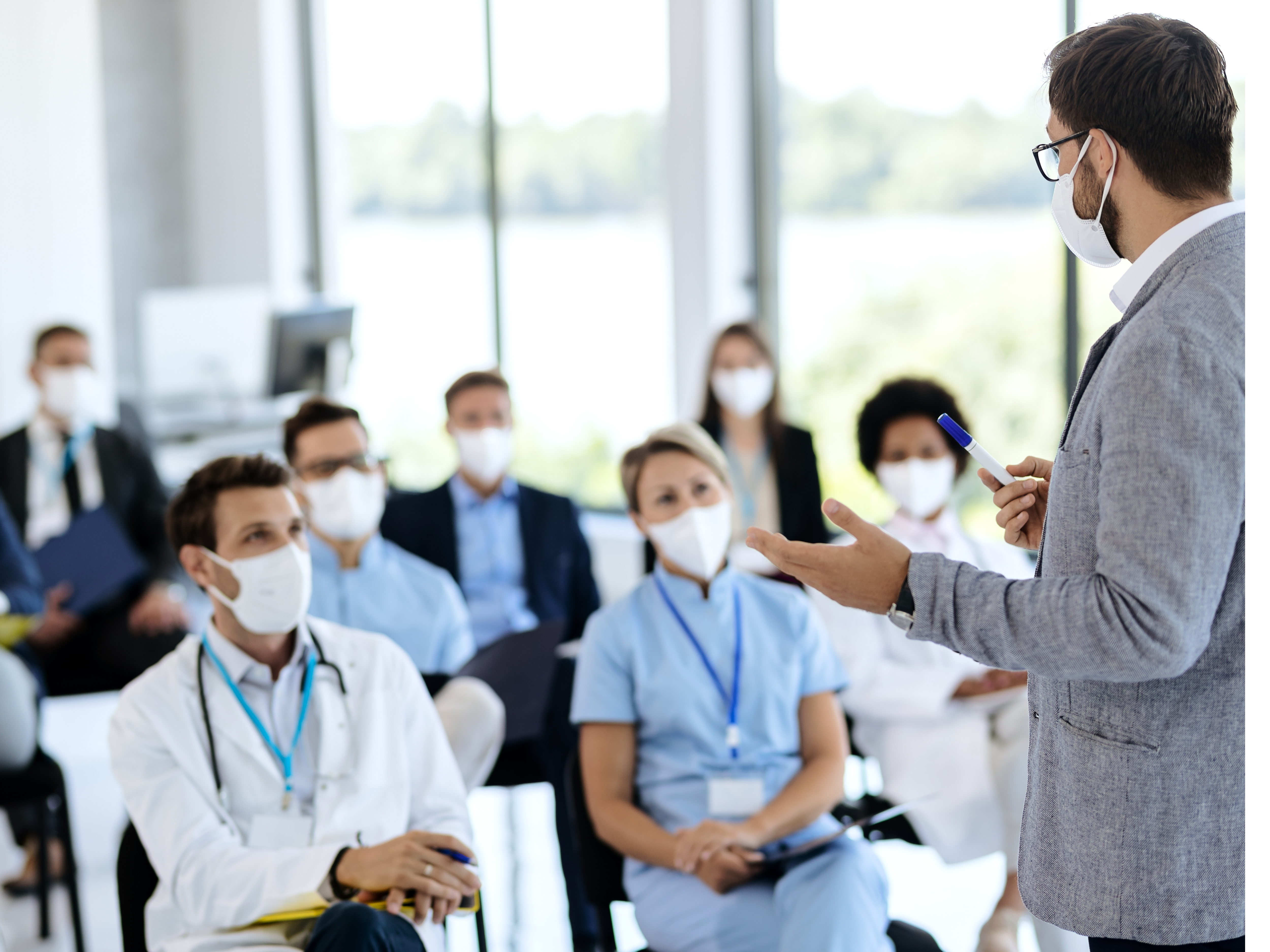 Physicians wearing masks, sitting in a room and listening to a speaker.